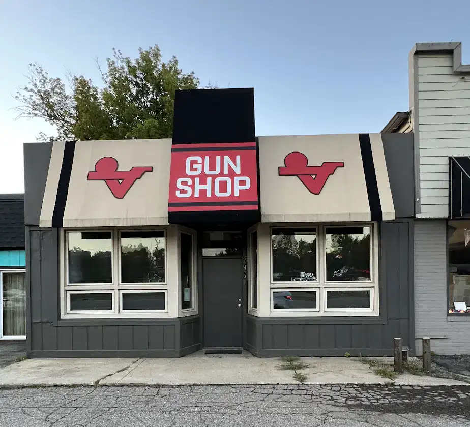 Outside of a gunshop in Highland Michigan. Gray building with beige and black awnings.